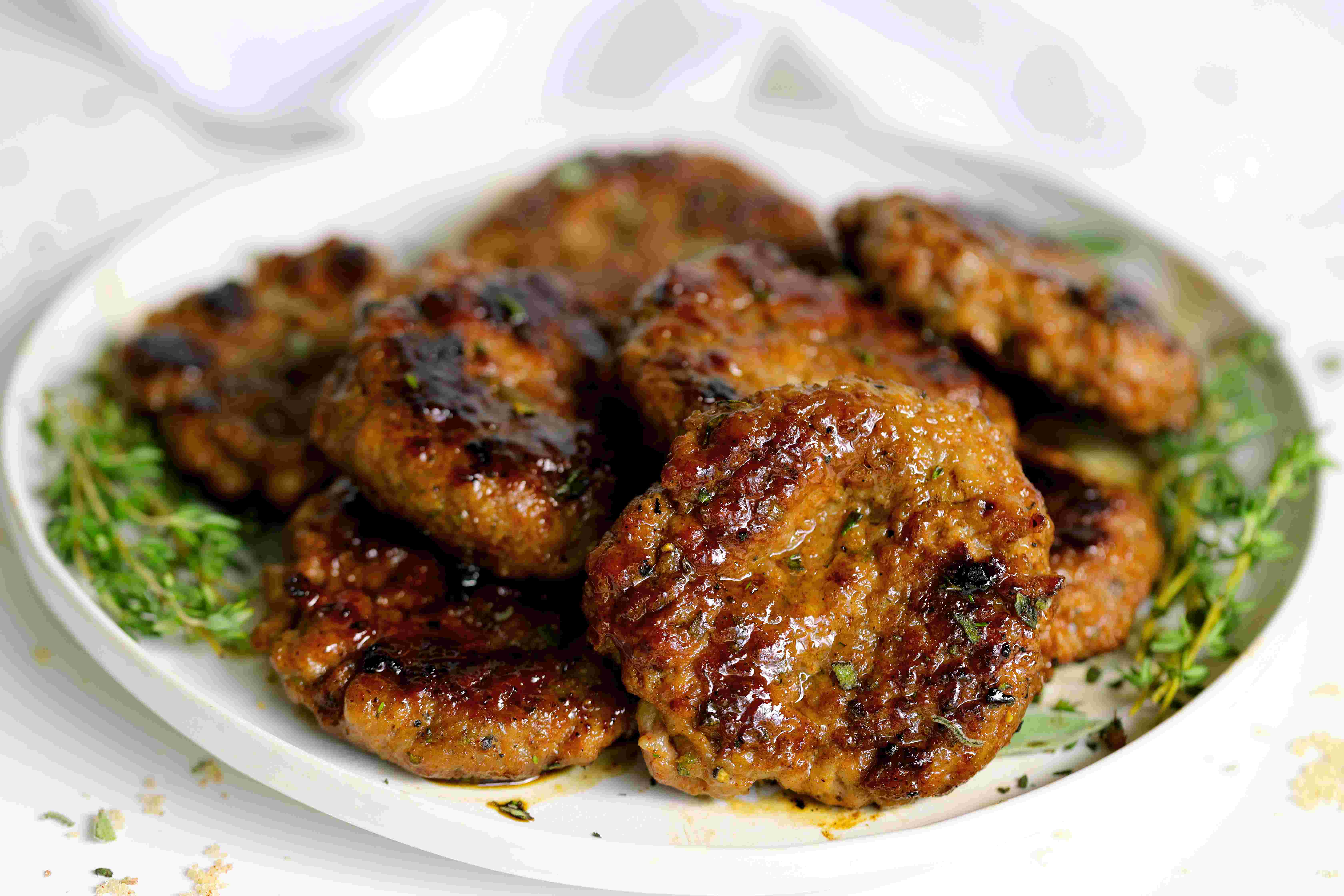 Prepared breakfast sausages on a white plate with fresh thyme