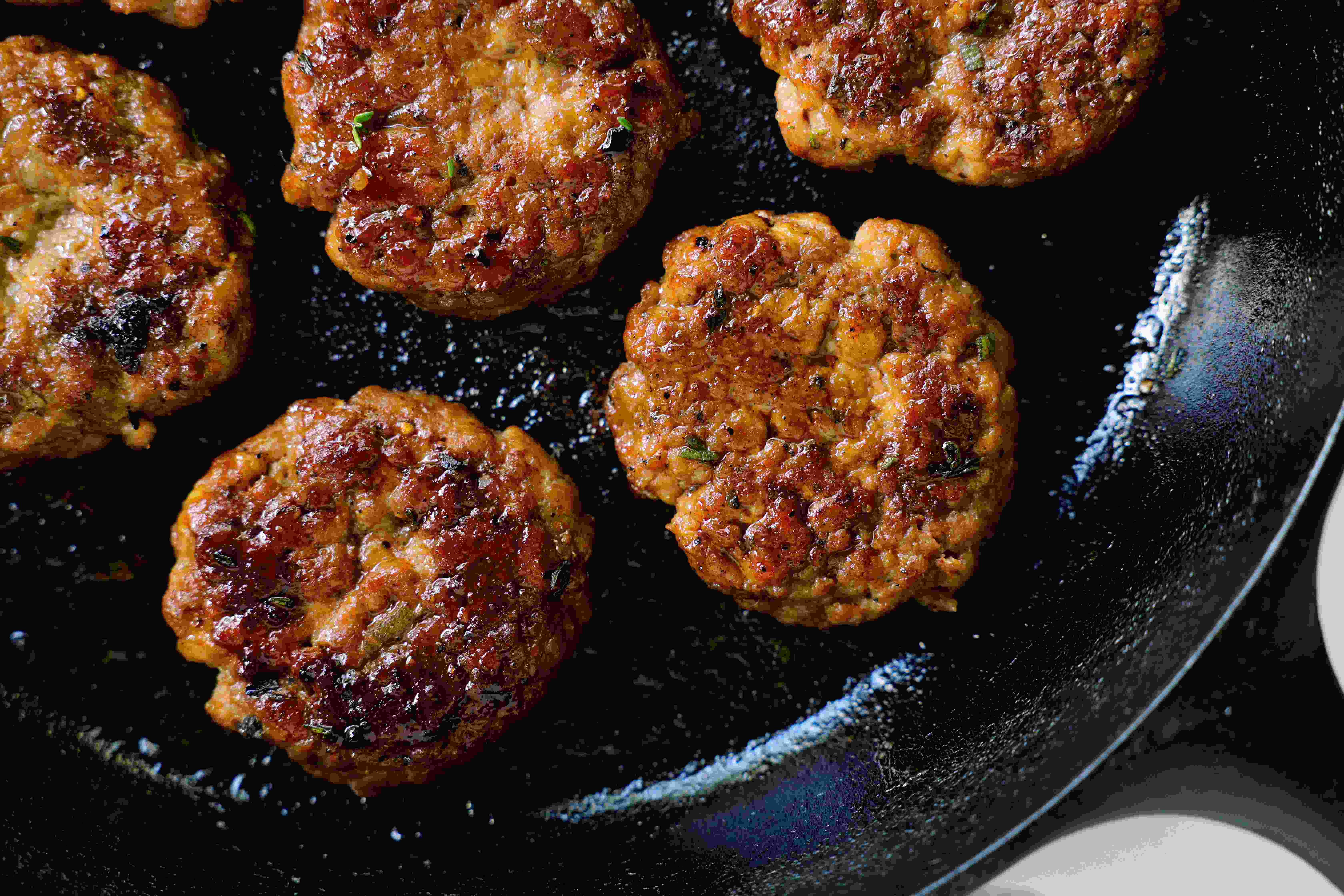 Six browned breakfast sausages cooking in a cast iron skillet