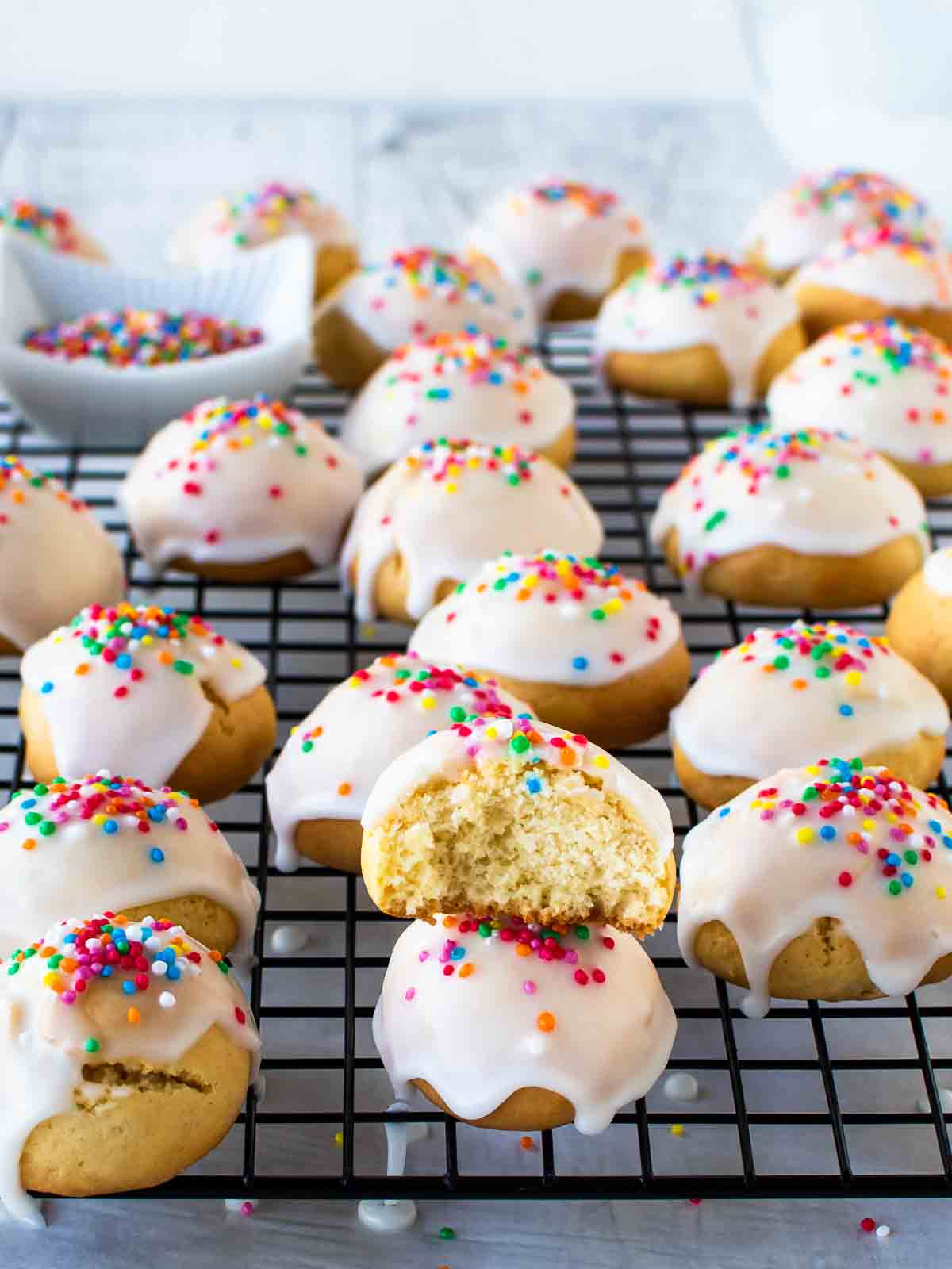 Italian Anise Cookies on black wire rack with one stacked cookie with bite taken.